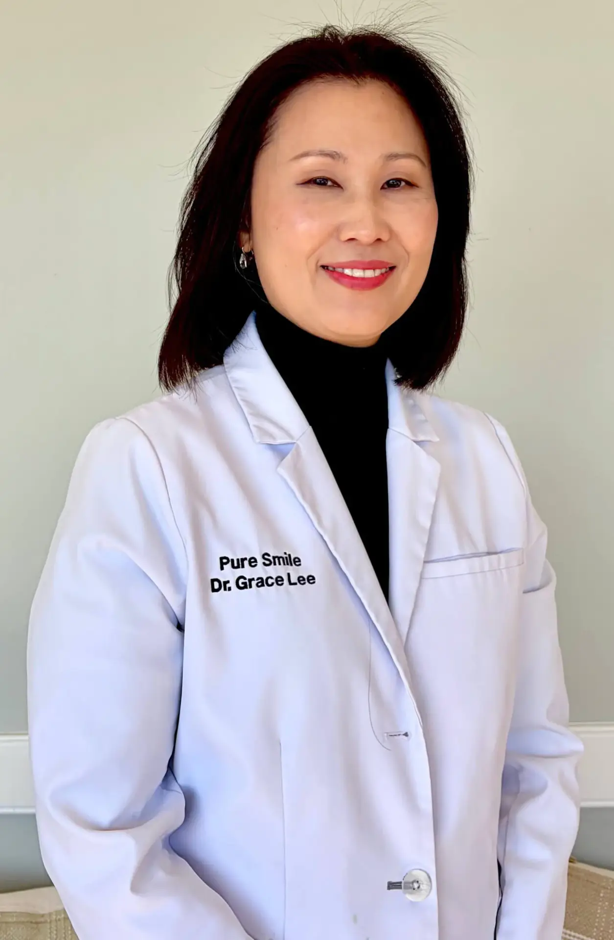 Dr. Grace Lee in white dental coat with "Pure Smile" branding, smiling in a professional setting, representing expertise in prosthodontics and patient care at Pure Smile Dentistry.