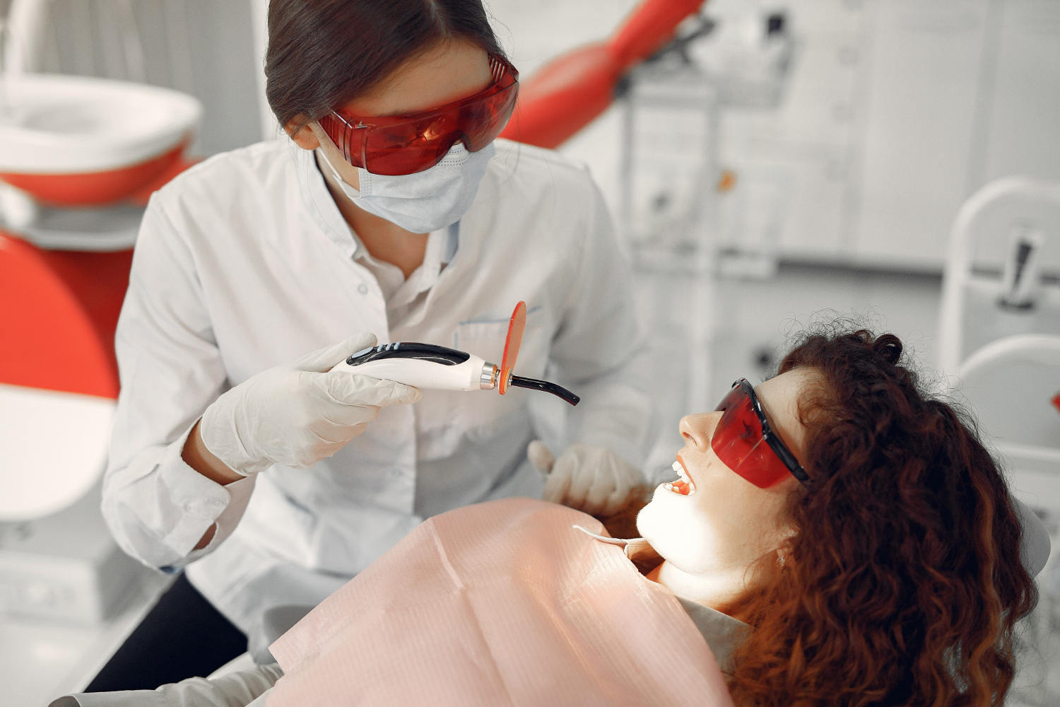 Dentist performing professional teeth whitening treatment on a patient wearing protective eyewear.