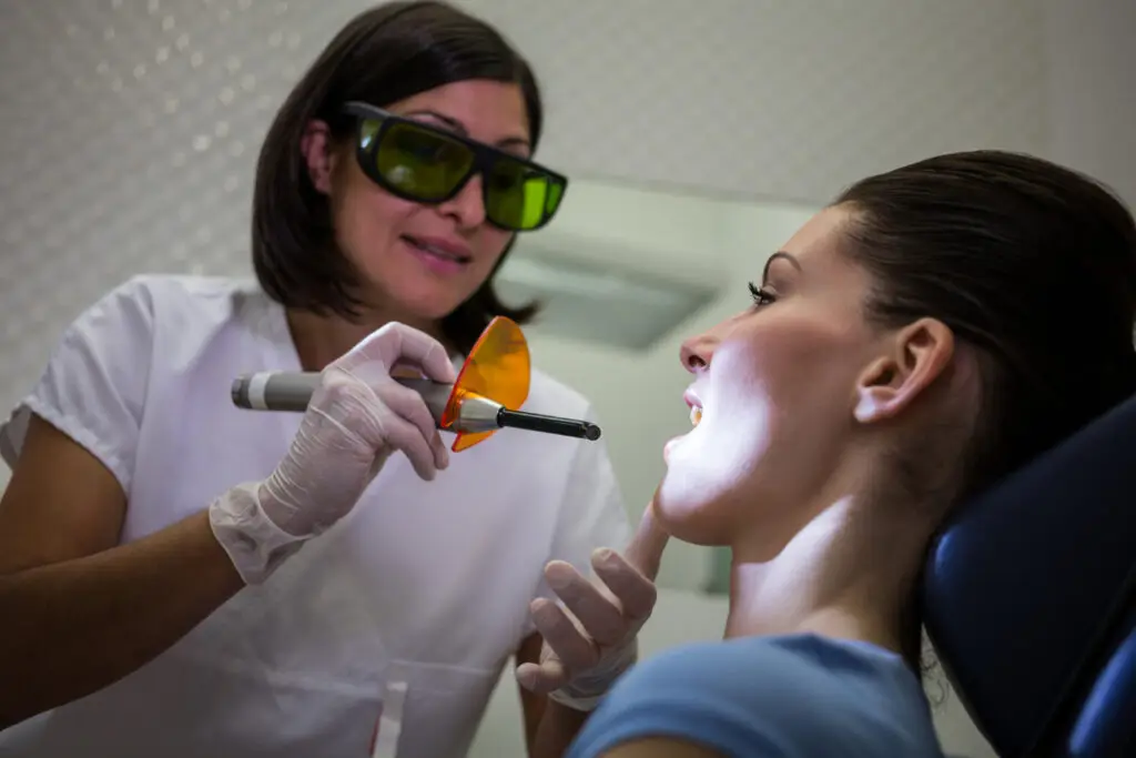 Dentist performing professional teeth whitening treatment on a patient in a dental office.