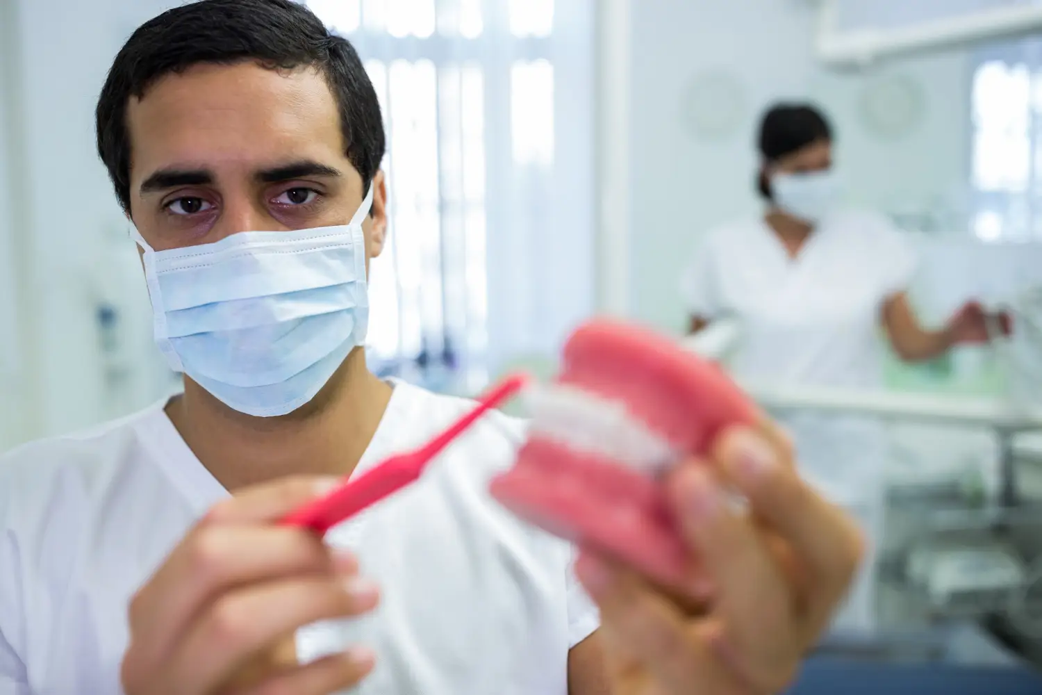 Dentist wearing a protective mask and holding a dental model and toothbrush in a clinic.