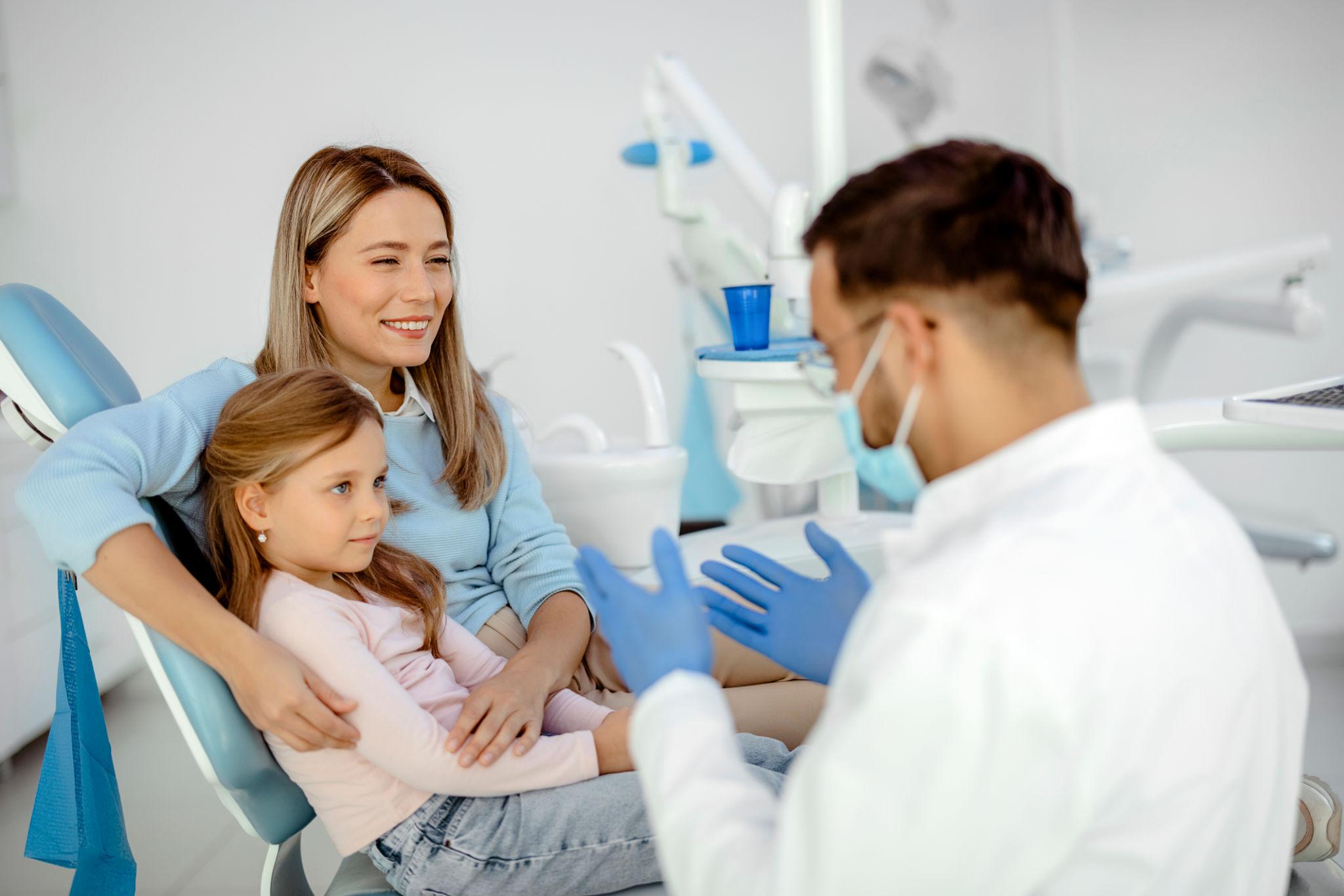 Pediatric dentist discussing dental care with a child and parent during a family dental consultation.